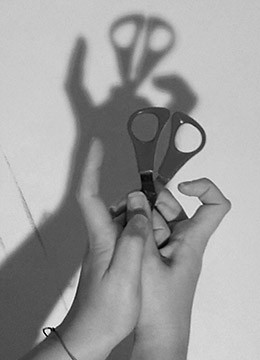 Ένα ζευγάρι χέρια κρατούν ένα ψαλίδι σχηματίζοντας σκιά